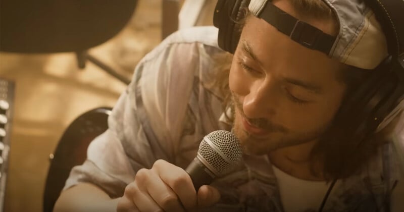 A man in headphones and a hat sings into a microphone. They are filmed from an overhead angle, focused and engaged in performance.