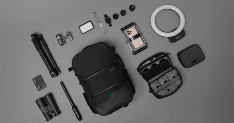 A collection of photography tools arranged on a gray background. Includes black bag, binoculars, camera tripod, lens kit, smartphone gimbal, LED ring light, small carrying case and various camera accessories.